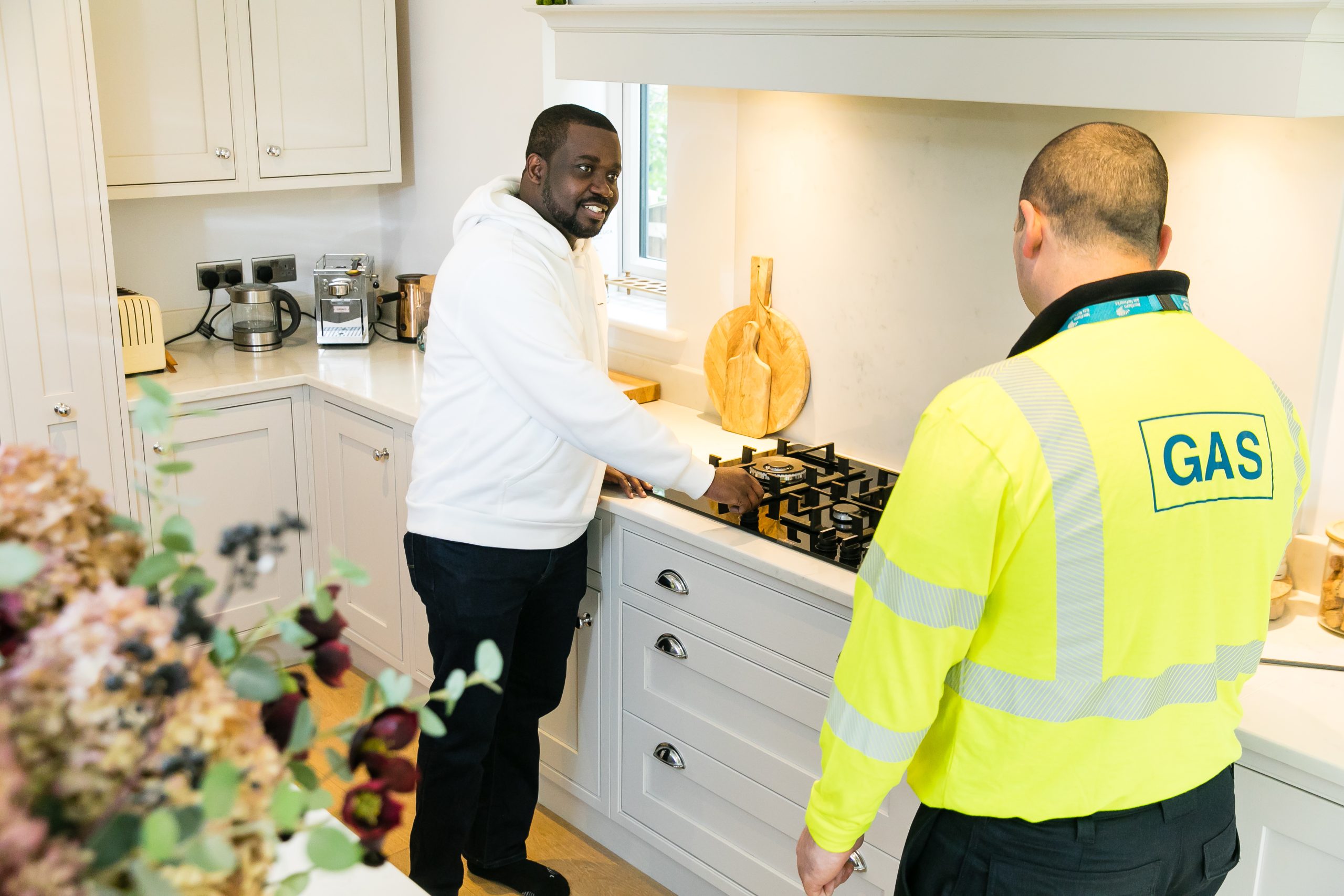 A man in his kitchen showing his gas hob to a gas engineer in a high vis jacket